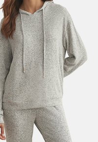 Haut à capuche gris clair en tissu doux. Présente une capuche, des manches longues et une coupe ample. Comprend des cordons de serrage avec des accents métalliques.