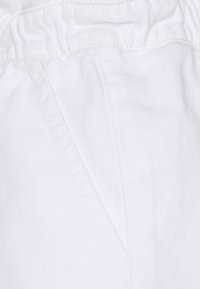 Tela blanca con una textura sutil, que presenta una cinturilla fruncida y acentos de costura. La vista de cerca enfatiza los detalles del material.