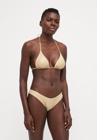 Μπουστάκι μπικίνι από αδιάφορο ύφασμα, με τριγωνικό σχέδιο και λεπτές τιράντες, συνοδευόμενο από χαμηλοκάβαλο σλιπ. Απλή σχεδίαση χωρίς μοτίβα ή αξεσουάρ.