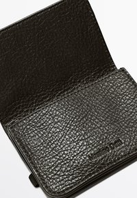 Sort læderpung med tekstureret finish og et præget logo, åben så man kan se designet af det indvendige rum.