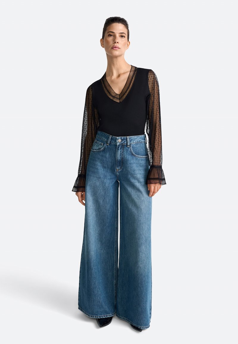 Zwarte bodysuit met doorzichtige, gestreepte lange mouwen, gecombineerd met high-waisted, wijde blauwe jeans en zwarte hoge hakken.
