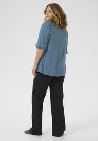 Blue textured blouse with puffed sleeves and a loose fit, paired with black wide-leg trousers. Minimal detailing, flat design.