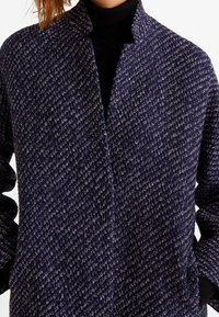Marineblå vævet frakke med et tekstureret fiskebensmønster, der har en mandarinkrave og to sidelommer.