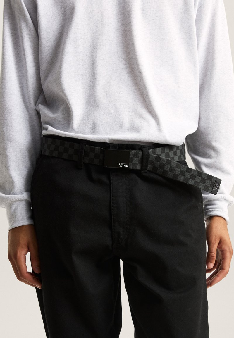 Black checkered belt with a rectangular buckle, featuring a Vans logo. Worn over black pants, paired with a light gray long-sleeve shirt.