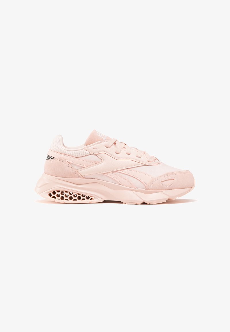 Baskets de sport rose clair avec un design à lacets, une semelle intermédiaire à motif nid d'abeille près du talon, et un logo discret sur le côté et la langue.