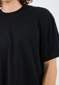 T-shirt noir à col rond fabriqué en coton. Manches courtes, coupe décontractée et texture lisse sans motifs ni accents visibles.