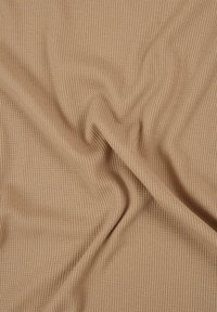 Tissu beige en maille gaufrée avec des plis doux et un motif en grille texturé, montrant un drapé naturel et de légères rides.