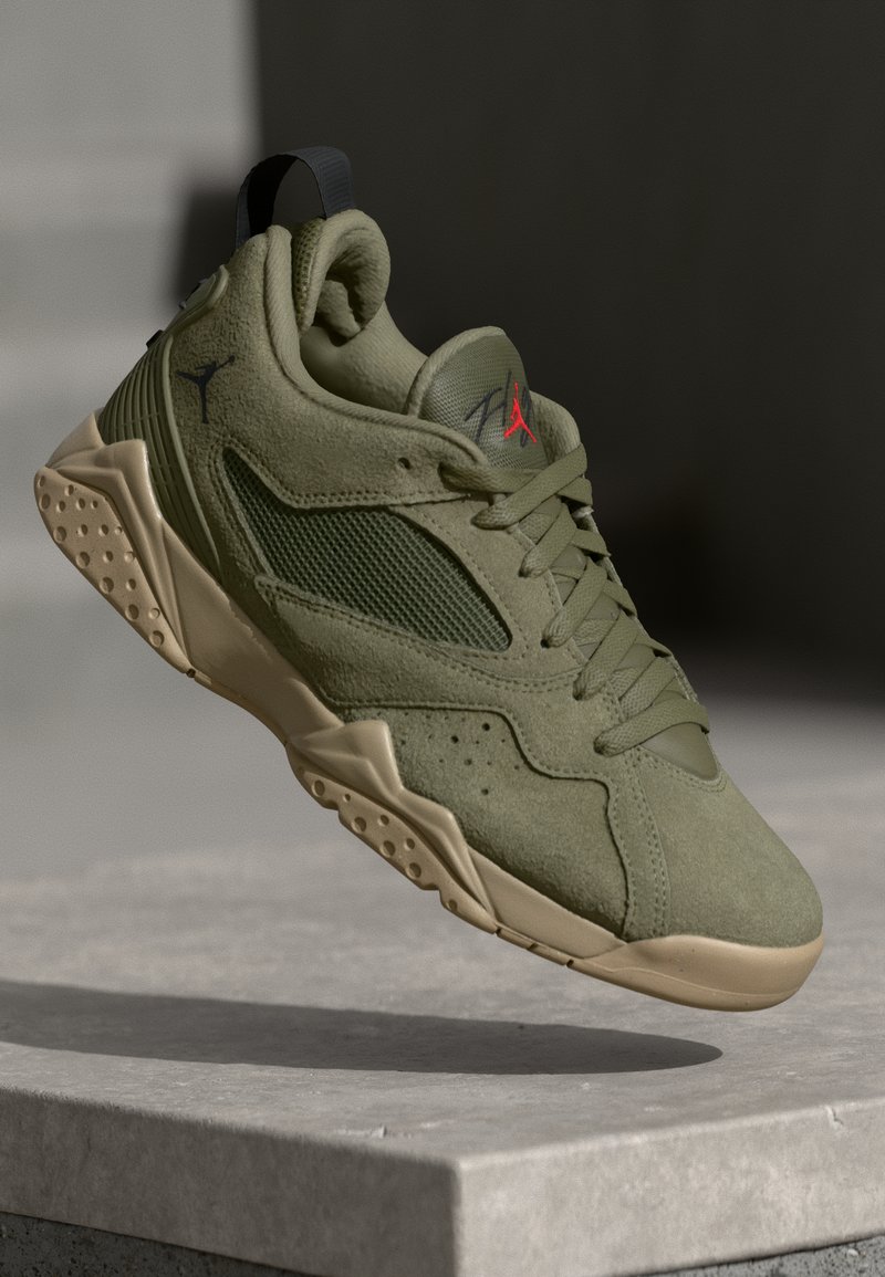 Sneaker in suede e mesh verde oliva con suola beige e logo Jumpman rosso, mostrato fluttuante sopra una superficie di pietra con ombra sottostante.