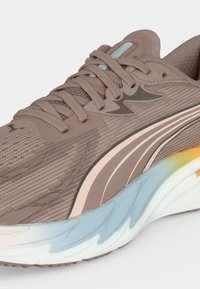 Αθλητικό παπούτσι ανοιχτό καφέ με περίπλοκο άνω μέρος από δίχτυ, ριγωτό πλαϊνό σχέδιο και χοντρή λευκή σόλα με μπλε και κίτρινες λεπτομέρειες.