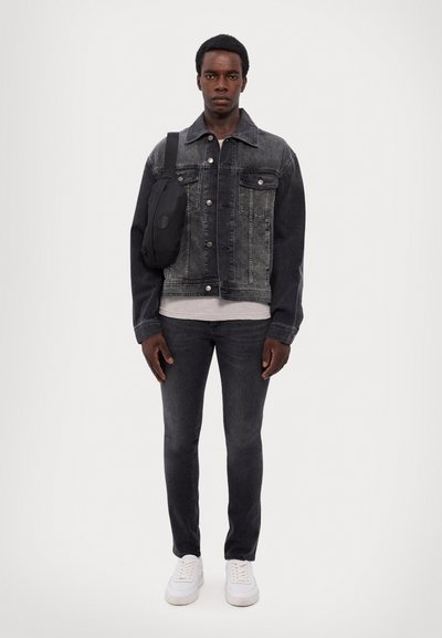 Veste en denim gris foncé avec des boutons métalliques, associée à un T-shirt gris, un jean skinny noir et des baskets blanches. Sac bandoulière noir.
