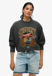 Grijze sweatshirt met een kleurrijk grafisch ontwerp van een strandscène met bloemen. Lichtblauwe versleten denim shorts met een rafelige zoom.