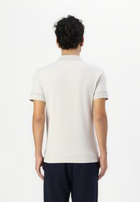 Beige Polohemd mit Kragen und kurzen Ärmeln, ausgestattet mit dezentem Markenaufdruck auf dem Ärmel, aus weichem, glattem Stoff gefertigt.