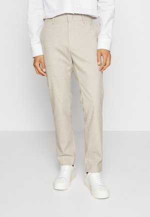 Beige trousers made of lightweight fabric, featuring a straight leg design. Paired with white sneakers and a cropped, striped white shirt.