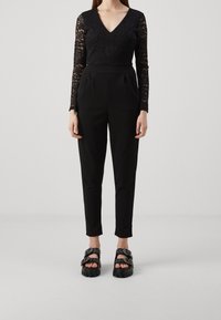 Svart spets långärmad topp med V-ringning och svarta högmidjade byxor. Matchas med kraftiga svarta sandaler med spännen.