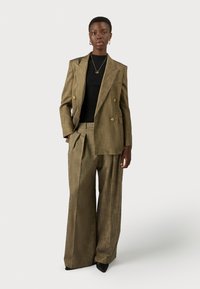 Dubbelbreasted bruine blazer met gouden knopen, gecombineerd met wijde geruite broek. Een zwarte getailleerde top en puntige zwarte schoenen maken de look compleet.