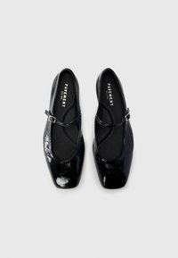 Black patent leather Mary Jane flats with a square toe, featuring a slim adjustable strap and smooth inner lining.