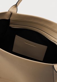Intérieur d'un sac à main en cuir beige avec doublure en tissu noir, poche zippée et étiquette cousue avec le nom de la marque embossé.
