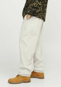 Lys grå sweatpants med løs pasform og elastiske manchetter, parret med brune, snørebåndsstøvler. Materialet ser blødt og struktureret ud.