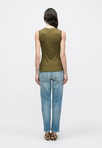 Top sin mangas de color verde oliva, diseño ajustado, combinado con jeans azul claro de pierna recta y calzado con estampado de leopardo, visto desde atrás.