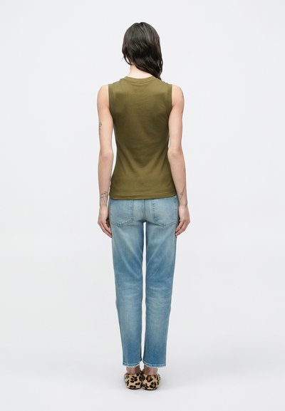 Αμάνικη μπλούζα σε ελιά πράσινο, στενή γραμμή, συνδυασμένη με φωτεινό γαλάζιο τζιν με ίσια γραμμή και παπούτσια με λεοπάρ σχέδιο, εμφανιζόμενα από πίσω.