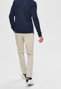 Beige kalhoty s rovný fit a hladkou texturou, doplněné tmavě modrou mikinou, obuté s bílými teniskami. Zadní pohled na outfita.