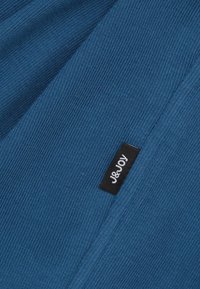Blauwe gebreide stof met een gladde textuur heeft een herkenbaar zwart label met witte tekst, waarop de merknaam "J&JOY" staat.