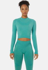 Top corto sportivo teal con maniche lunghe e vita a taglio, caratterizzato da pannelli texturizzati e una vestibilità aderente. Leggings coordinati a vita alta.