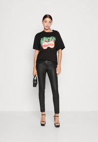 Melna grafiska T-kreklu ar krāsainu zobu dizainu, apvienota ar melnām pieguļošām ādas biksēm un melnajiem siksnu papēžiem. Mazs melns rokassomu.