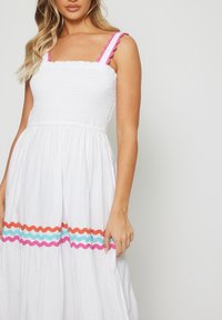 Abito bianco con corpino arricciato, spalline rosa a scallop e un motivo zigzag colorato in arancione, blu e rosa all'orlo.
