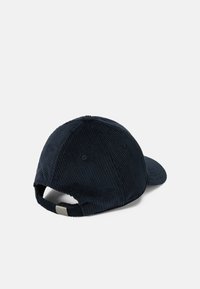 Gorra de pana azul marino con visera curva, superficie texturizada, correa trasera ajustable y un detalle metálico cerca de la abertura.