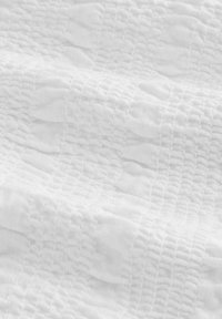 Tissu blanc texturé avec une grille en relief et un motif ondulé subtil, montrant des plis et des ombres légères.