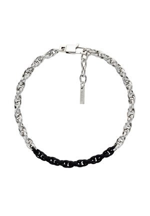 Collier en chaîne argentée avec un segment à maillons noirs et une petite étiquette USPA suspendue à l'extension réglable du fermoir.