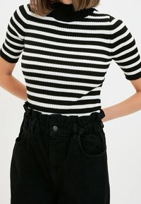 Haut rayé noir et blanc à manches courtes avec un col montant, associé à un pantalon noir taille haute avec un ceinture froncée.