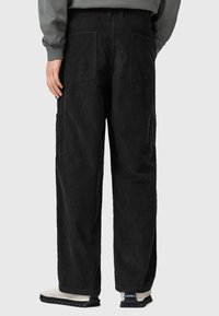 Pantaloni cargo neri in corduroy con una vestibilità rilassata, dotati di tasche laterali e un motivo a coste texturizzato, abbinati a una felpa grigia e calzature.