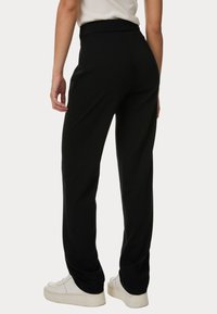 Pantaloni neri a gamba larga con vita alta, tessuto morbido e drappeggio sottile, abbinati a sneakers bianche.