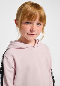 Lichtroze hoodie met een voorzak, voorzien van zwarte zijaccenten en logo-tekst. Zachte stof met een ontspannen pasvorm en een capuchon met trekkoord.