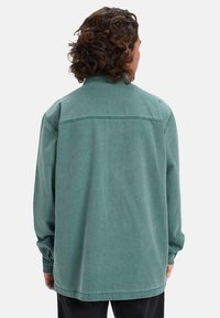 Green, long-sleeve shirt in a relaxed fit, featuring a soft, textured fabric, straight hem, and minimalistic design with back yoke detail.