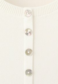 Gros plan sur un tissu blanc côtelé avec quatre boutons ronds, brillants, à deux trous, alignés verticalement sur un vêtement en tricot.