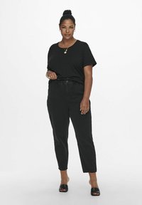 Black crew-neck t-shirt, paired with black high-waisted tapered jeans. Black slip-on sandals. Simple accessories, hair tied back. Minimalist style.