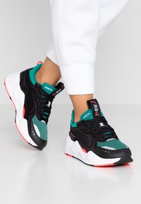 Svarta och teal sportiga sneakers i mesh och läder, med en djärv design, vit mellansula och rosa accenter.