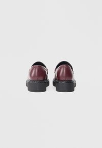 Burgundy läderskor med en slät yta, rund tå och låg svart plattformssula. Bakifrån syns böjda sömmar och design för att enkelt sätta på sig skorna.