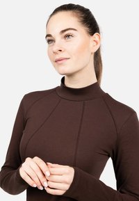 Hnědý dlouhý rukáv s lichotivým límcem, který má přiléhavý střih, jemné šití a hladkou texturu látky.