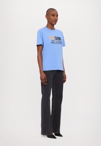 Gaiši zilā T-kreklā ar melniem un oranžiem uzrakstiem, apvienots ar tumši pelēkām platām džinsām. Vienkārša dizaina, īsām piedurknēm un brīvi pieguļoša.