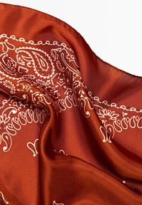 Bandana en soie dans un riche rouille avec des motifs paisley et floraux blancs, présentant une texture lisse et des bords finement cousus.