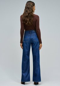 Pantalones vaqueros de denim azul de cintura alta con un diseño de pierna ancha, que cuentan con una textura suave y un estilo clásico de cinco bolsillos.