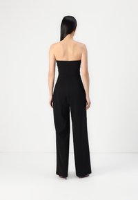 Svart strapless jumpsuit med tettsittende bodice og vide bukser. Glatt tekstur med skjult glidelås bak.