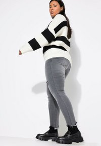 Jersey a rayas blanco y negro con corte holgado, combinado con jeans skinny grises rasgados y mocasines negros de plataforma. Textura suave, estilo casual.