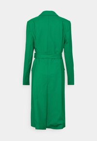 Groene trenchcoat met een lange silhouet, dubbele knopen en een stoffen riem. Opvallende kenmerken zijn de klassieke kraag en de soepele textuur.