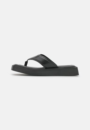 Sandale à plateforme noire avec une semelle épaisse et une large bride en cuir sur le pied, montrée de profil sur un fond uni.