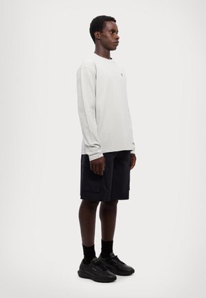 Long-sleeve light gray shirt paired with black shorts. Textured fabric and a subtle logo on the shirt. Black sneakers complete the look.
